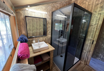 Salle de bains d'une Safari Tent XXL avec cabine de douche moderne et murs en bois au Flower Camping de la Trye, France.