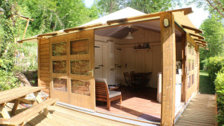 Lodge Bali wooden cabin with open front, deck, and picnic table, surrounded by lush green foliage.