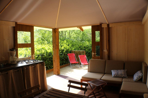 Vista interna della Lodge Bali al Campeggio Moulin de Chaules, Francia, con cucina, divano e terrazza esterna.