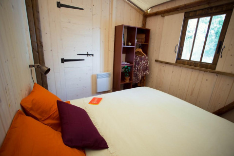 Accogliente camera da letto nella Lodge «Bali» al Campeggio Moulin de Chaules con pareti in legno.