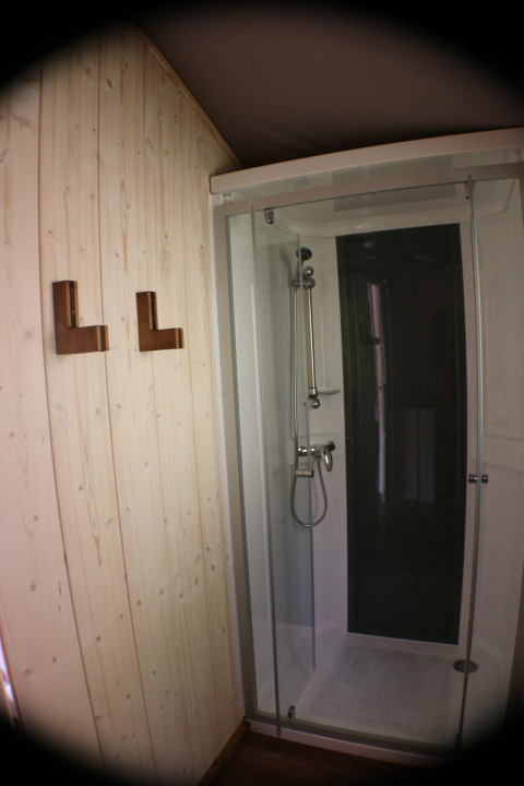 Doccia con porta di vetro e parete in legno con ganci presso Lodge «Bali», Campeggio Moulin de Chaules, Francia.