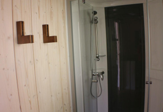 Douche met glazen deur en houten wand met haken in Lodge «Bali» op Camping Moulin de Chaules, Frankrijk.