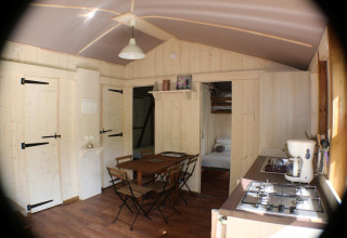 Interno della Lodge «Bali» al campeggio Moulin de Chaules, legno chiaro e zona pranzo accogliente.