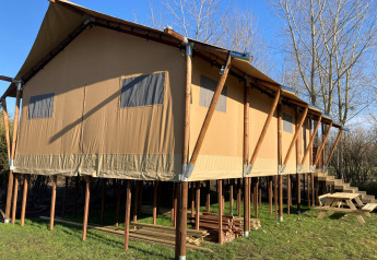 Large safari tent on stilts with windows at Flower Camping de la Trye in France, sunny clear day view.