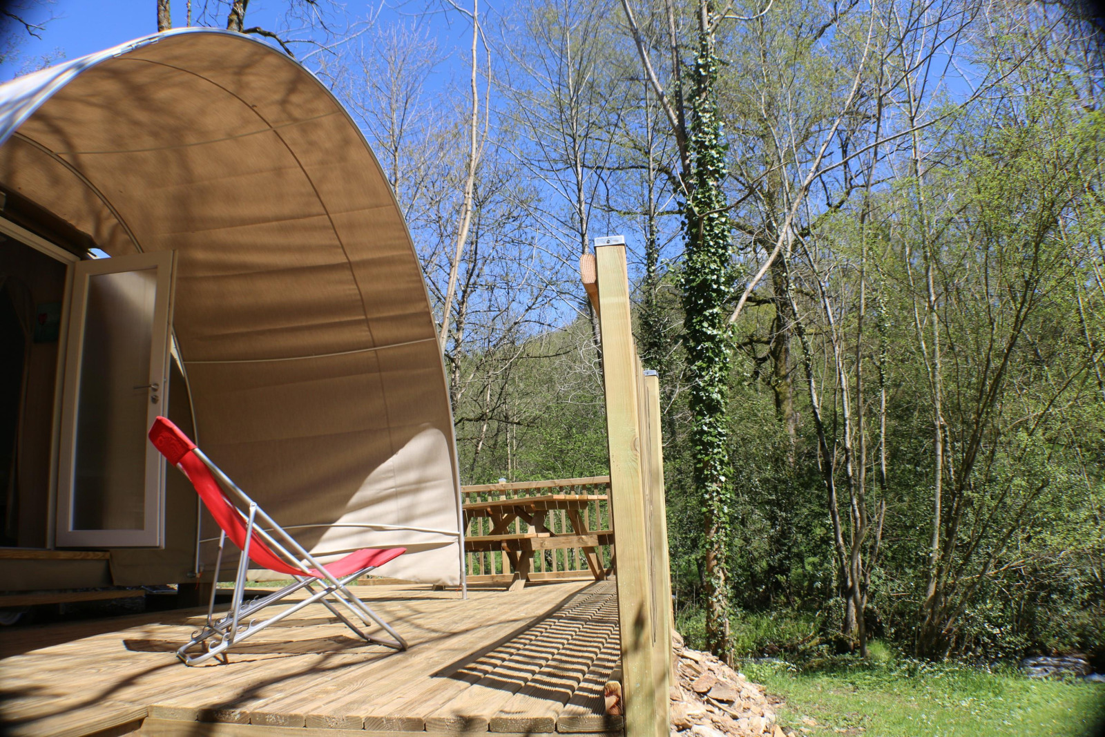 Zonnig terras met rode ligstoel voor CocoSweet safaritent op camping Moulin de Chaules, Frankrijk.