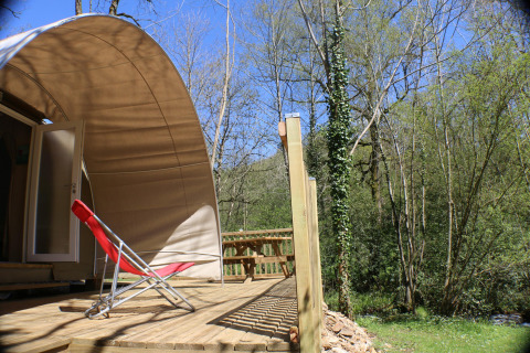 Terrazza soleggiata con sedia a sdraio rossa davanti a tenda CocoSweet al campeggio Moulin de Chaules, Francia.