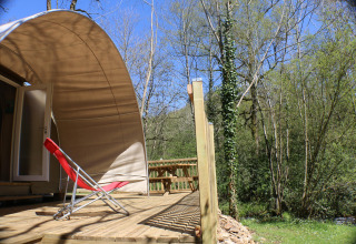 Terrazza soleggiata con sedia a sdraio rossa davanti a tenda CocoSweet al campeggio Moulin de Chaules, Francia.