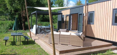 Terras van Luxe Lodge met buitenzitje, jacuzzi, picknickbank en groene omgeving in de zon.