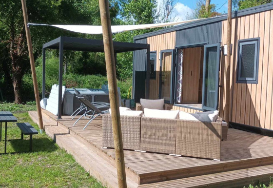 Terras van Luxe Lodge met buitenzitje, jacuzzi, picknickbank en groene omgeving in de zon.