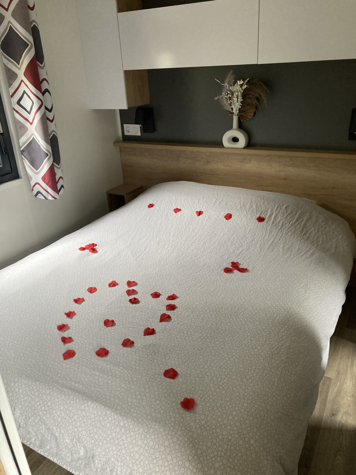 Lodgekamer met een wit bed, versierd met rode rozenblaadjes in de vorm van een hart op het dekbed.