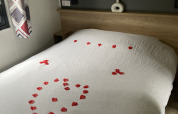 Lodgekamer met een wit bed, versierd met rode rozenblaadjes in de vorm van een hart op het dekbed.