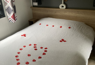 Lodgekamer met een wit bedlaken en rode rozenblaadjes in hartvorm op het bed verdeeld.
