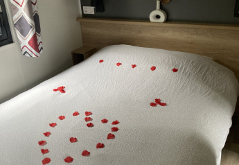 Bett in einer Lodge mit weißer Bettwäsche und roten Rosenblättern, die ein Herz auf dem Bett bilden.