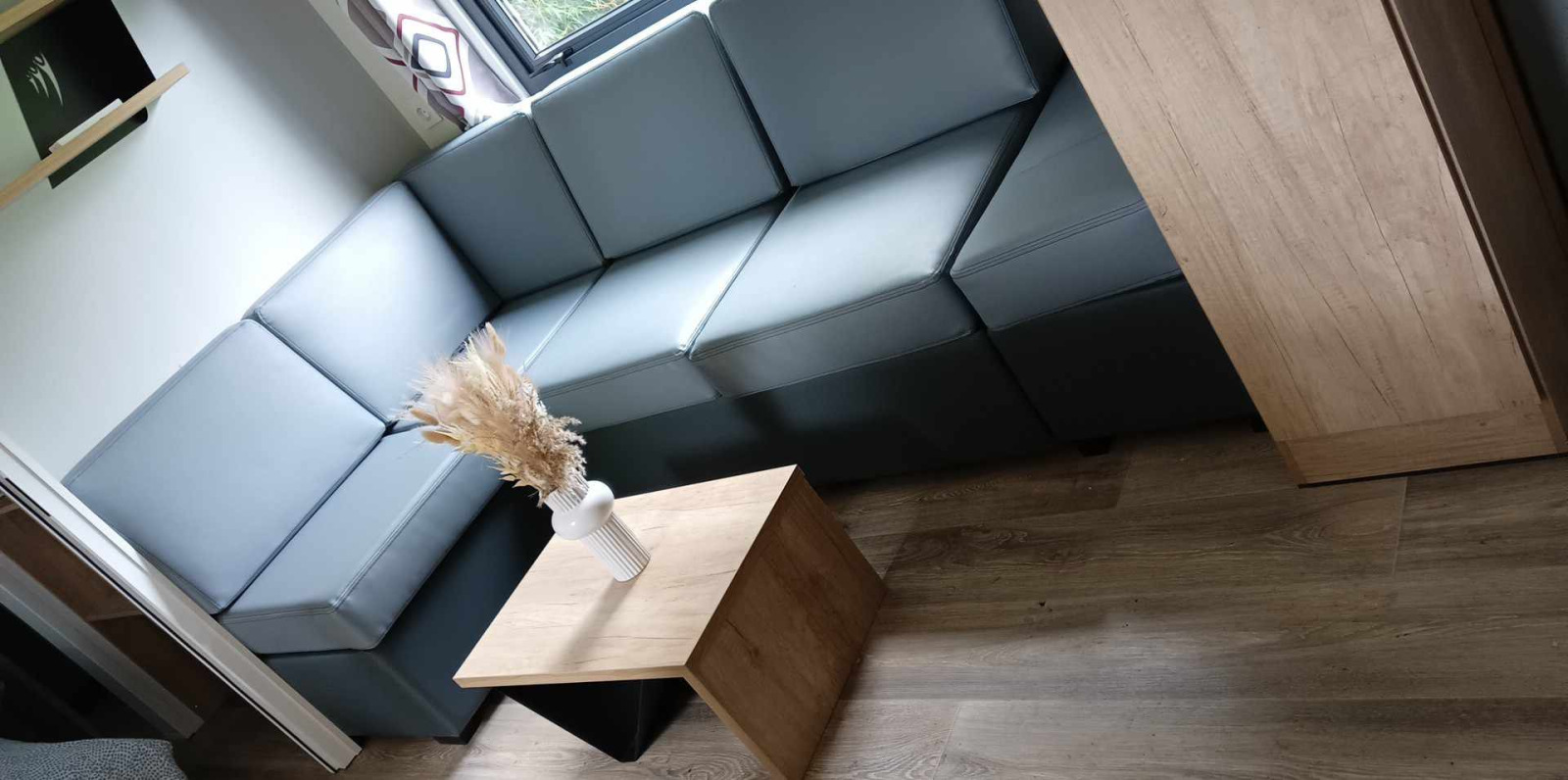 Moderne lodge-woonkamer met grijze hoekbank, houten tafeltje en vaas met gedroogde bloemen bij het raam.