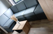 Moderne lodge-woonkamer met grijze hoekbank, houten tafeltje en vaas met gedroogde bloemen bij het raam.