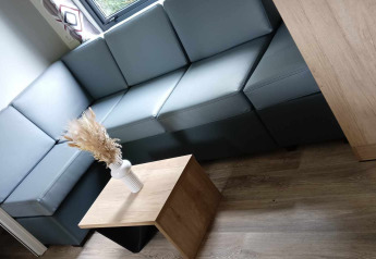 Soggiorno di lodge moderno con divano angolare grigio, tavolino in legno e vaso con fiori secchi vicino alla finestra.
