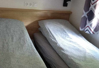 Two single beds with patterned duvets in a bright room at Luxe Lodge + jacuzzi, Flower Camping de la Trye, France.
