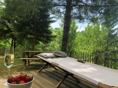Relaxing view from a safari tent deck with sunbed, pillows, picnic table, strawberries and sparkling wine.
