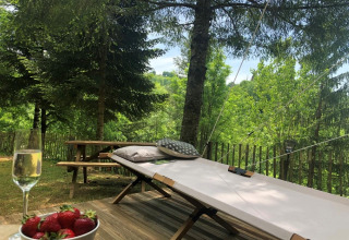 Relaxing view from a safari tent deck with sunbed, pillows, picnic table, strawberries and sparkling wine.