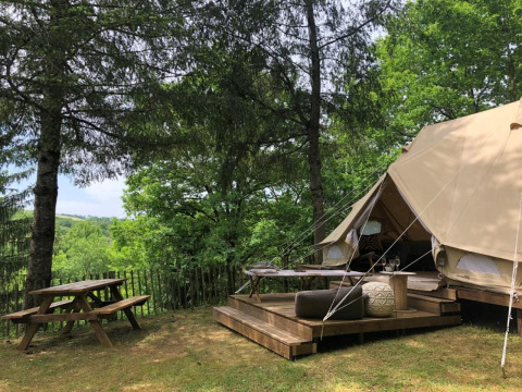 Safari experience in an Emperor Bell Tent with wooden deck and picnic table in a lush forest setting.