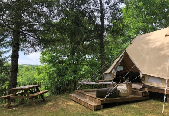 Safari experience in an Emperor Bell Tent with wooden deck and picnic table in a lush forest setting.