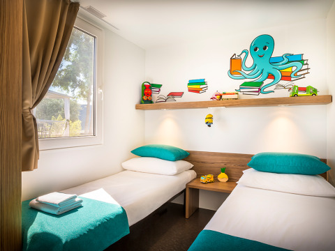Kinderkamer in een chalet met twee aparte bedden, turquoise kussens, speelgoed en een blauwe octopus op de muur.