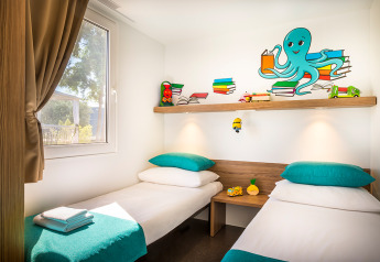 Kinderkamer in een hut met twee eenpersoonsbedden, kleurrijke kussens, speelgoed en een octopus muurschildering.