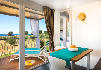 Interior luminoso de una cabaña con mesa de comedor y acceso a terraza con vistas al mar en Croacia.