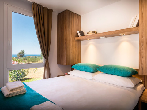 Moderne slaapkamer met dubbel bed, turquoise kussens en zeezicht op Aminess Maravea Resort in Kroatië.