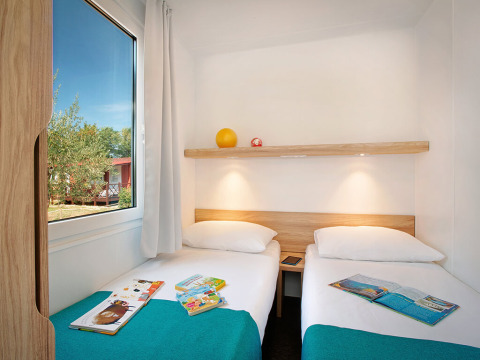 Moderne vakantiewoning met twee enkele bedden, boeken op het bed en zicht op de tuin in Kroatië.