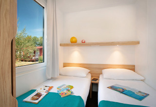Moderne vakantiewoning met twee enkele bedden, boeken op het bed en zicht op de tuin in Kroatië.