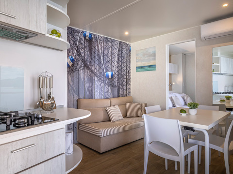 Modern cabine-interieur met open keuken, eettafel, bank en maritieme decoratie, licht en gezellig.