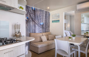 Modern cabininterieur met open keuken, eettafel, sofa en maritieme decoratie, helder en gezellig.