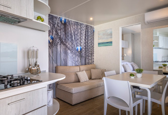 Interno cabina moderno con cucina a vista, tavolo da pranzo, divano e decorazioni nautiche, luminoso e accogliente.
