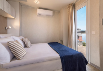 Camera di cabina moderna con letto matrimoniale, cuscini a righe, coperta blu e vista lago dalla porta.