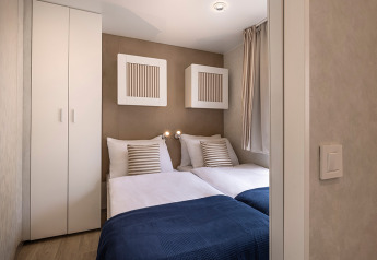 Piccola camera da letto in una cabina con due letti singoli, armadio bianco e coperte blu vicino alla finestra.