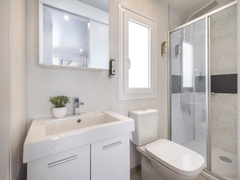 Lichte, moderne badkamer in een chalet met wastafel, toilet, spiegel, raam en glazen douchecabine met zwarte strook.