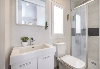 Bagno luminoso e moderno in una cabina, con lavabo, WC, specchio, finestra e box doccia in vetro con dettaglio nero.