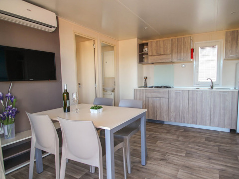 Coin salle à manger et cuisine moderne avec quatre chaises, bouteille de vin et TV dans un lodge Park Riviera au Camping Park Umag, Croatie.