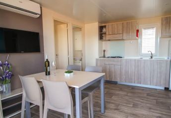 Coin salle à manger et cuisine moderne avec quatre chaises, bouteille de vin et TV dans un lodge Park Riviera au Camping Park Umag, Croatie.