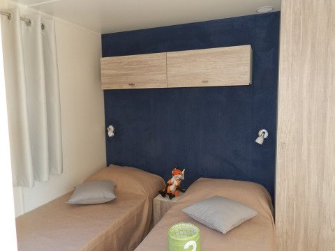 Bedroom with two single beds, blue accent wall and wooden cabinets at Park Riviera lodge, Campsite Park Umag, Croatia.