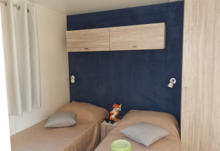 Bedroom with two single beds, blue accent wall and wooden cabinets at Park Riviera lodge, Campsite Park Umag, Croatia.