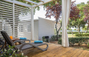 Sunny deck with loungers and garden view at Park Riviera «EVO» in Campsite Park Umag, Croatia, surrounded by trees.