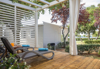 Sunny deck with loungers and garden view at Park Riviera «EVO» in Campsite Park Umag, Croatia, surrounded by trees.