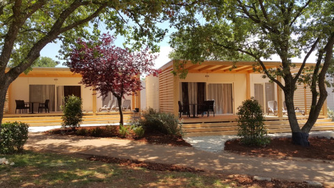 Deux lodges Park Riviera EVO au camping Park Umag en Croatie, entourés d’arbres et de terrasses en bois.