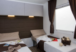 Modern lodge room at Park Riviera «EVO» in Campsite Park Umag, Croatia featuring three beds and large window.