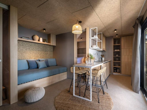 Modern lodge interior featuring a compact kitchen, dining area, cozy sofa, and woven natural accents.