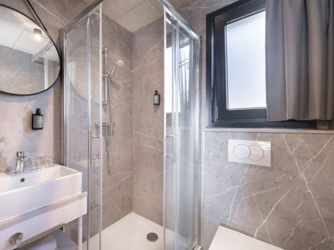 Moderne badeværelse på et lodge, med glasbrusekabine, hvid vask, stort vindue og grå fliser.