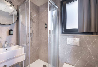 Modern lodge bathroom featuring a glass shower enclosure, white sink, large window, and marble tiles.