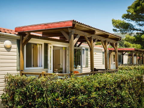 Cabañas Padova Home con porches de madera y setos verdes en Valamar Camping Padova, Croacia, día soleado.